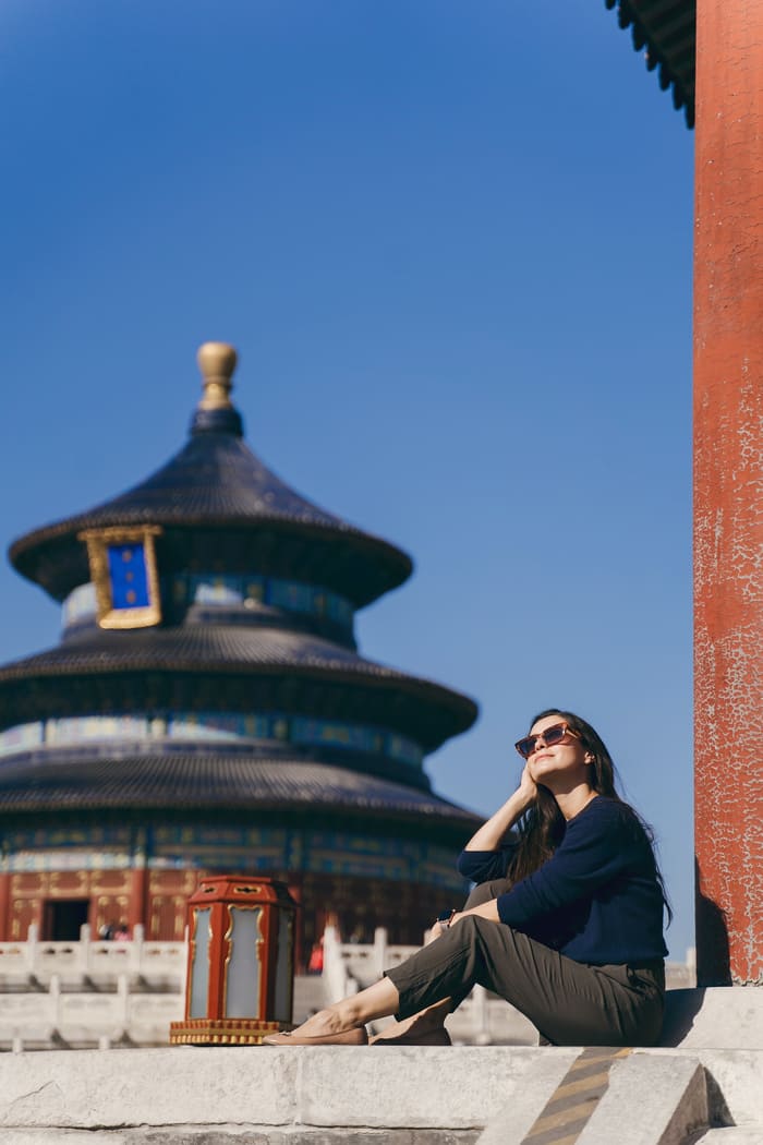 "Viajera sentada relajadamente en las escalinatas frente al icónico Templo del Cielo en Beijing, disfrutando de un día soleado durante su viaje a China