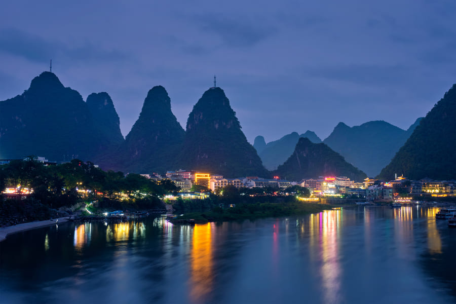 "Vista nocturna del paisaje de Yangshuo, China, con sus icónicas montañas kársticas iluminadas reflejándose en el río